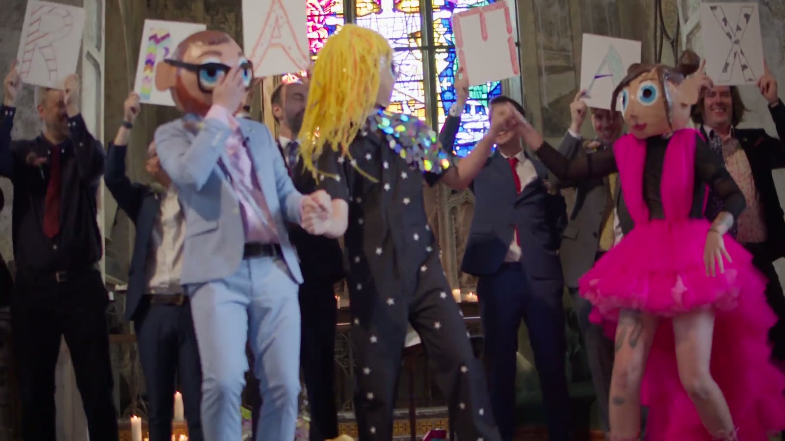 Wedding guests in bright outfits dancing outside a church