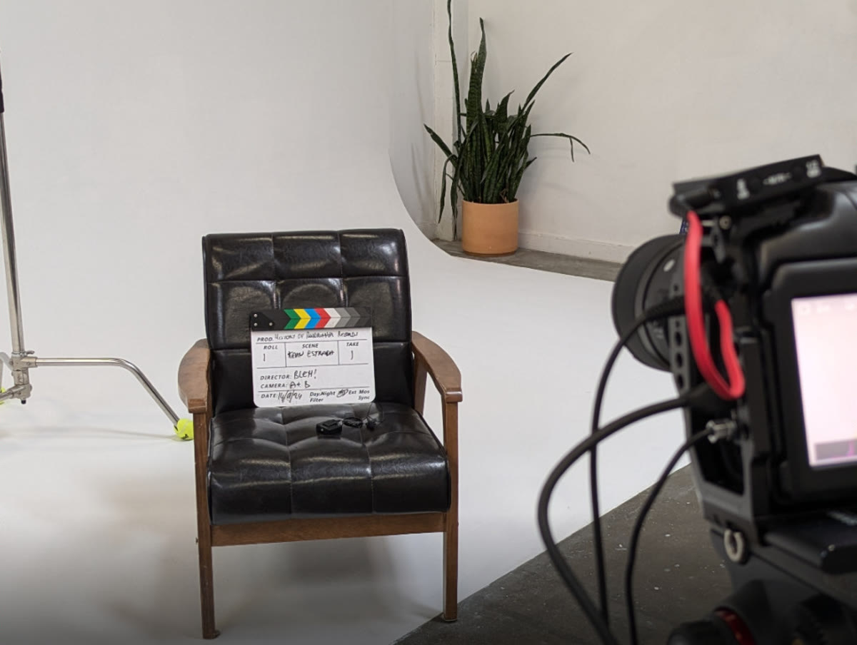 A film set: a leather chair with a clapperboard on it, a light stand, and a cinema camera in the foreground